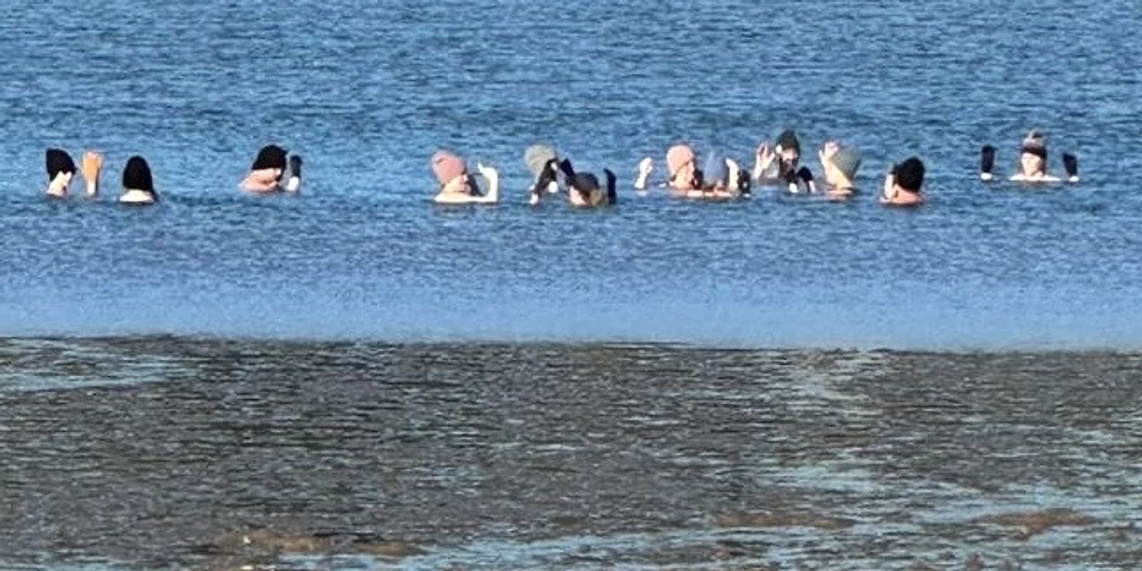 Un groupe de baigneurs en bonnets de laine pendant une baignade froide dans le lac d’Hossegor