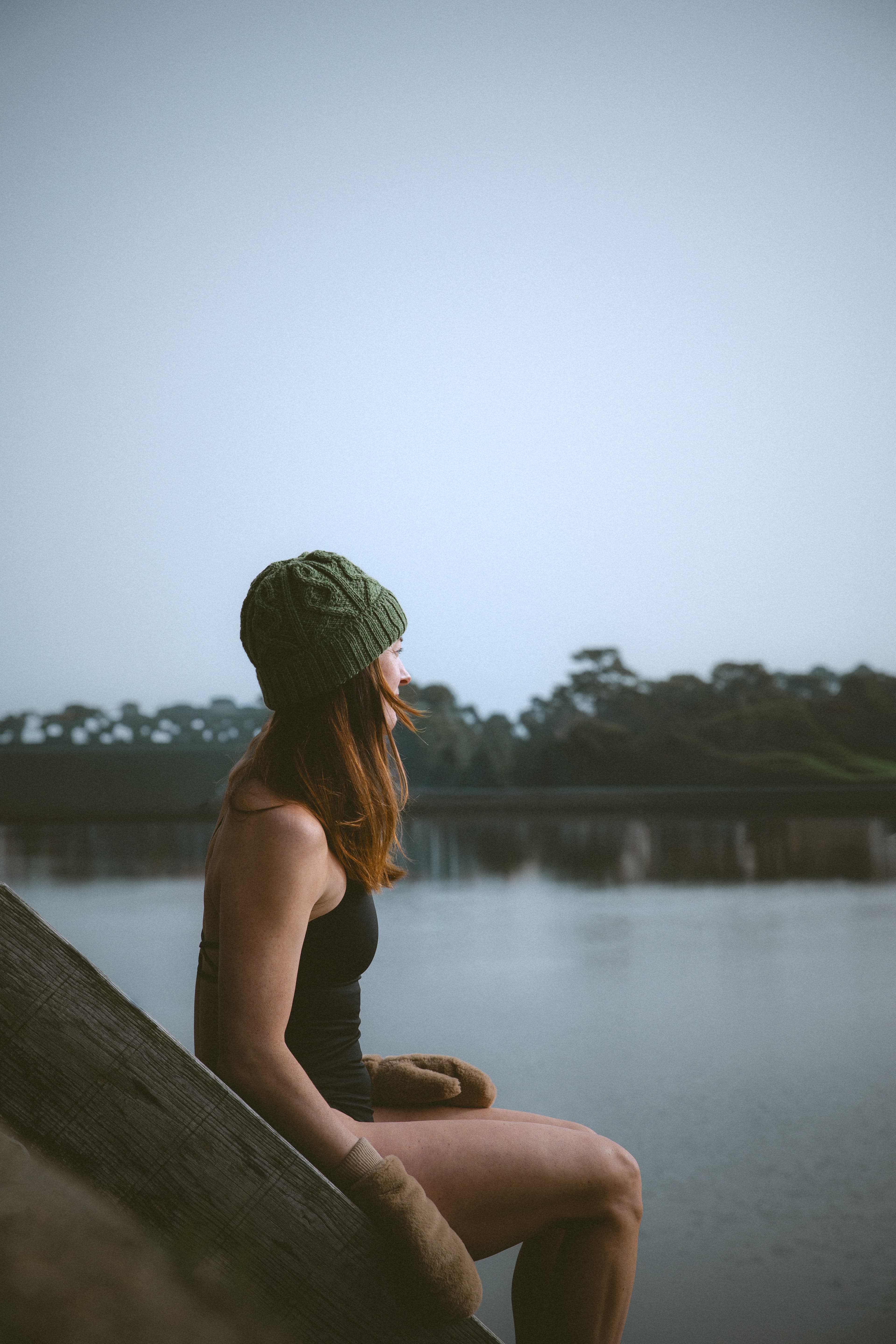 Aisling, fondatrice de Nomad Sauna & Ice, en bonnet vert assise sur un ponton en bois face au lac