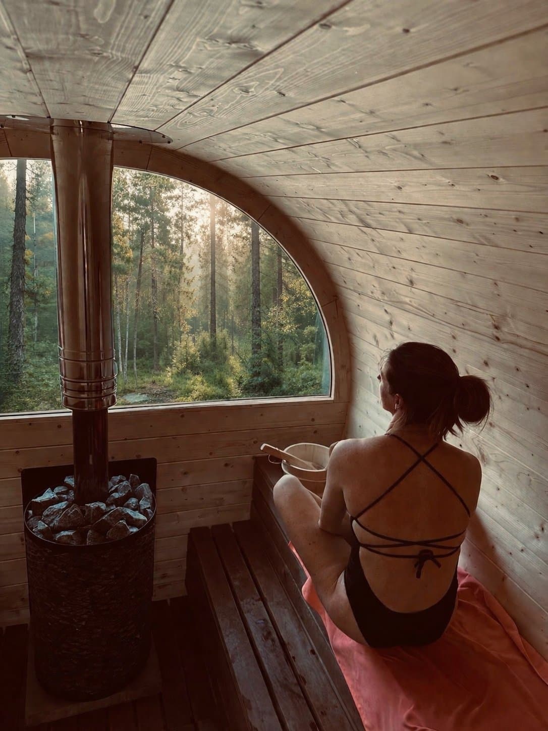 Bancs en bois et fenêtre sur la nature à l’intérieur du sauna tonneau Nomad